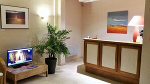 A reception area with a wooden desk, a potted plant, a television, and framed artwork on the walls. - Hotel Val De Loire (Azay-le-Rideau)