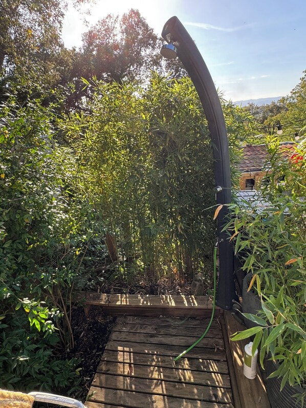 A wooden deck with a curved black structure, surrounded by dense foliage and a distant building.