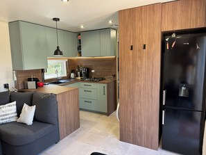 A modern kitchen with a built-in island, a black refrigerator, and a grey sofa with a white pillow.