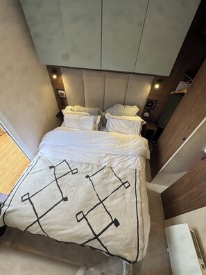 A bed with a patterned blanket, a headboard, bedside tables, and a wall-mounted air conditioning unit.
