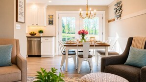Una cocina moderna con armarios blancos, un comedor con mesa y sillas de madera, y vistas a zonas verdes.
