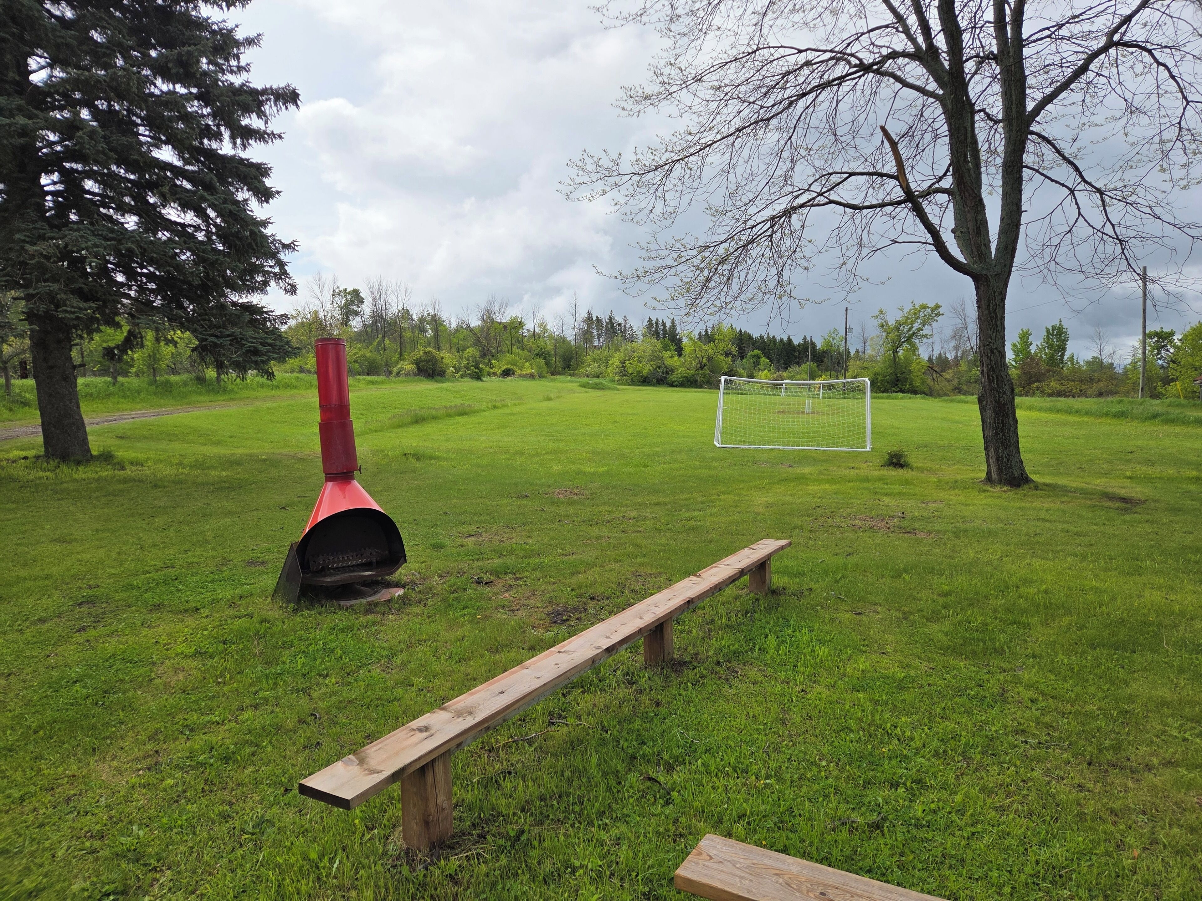 A grassy field with a wooden bench, a red chimney, and a soccer goal.