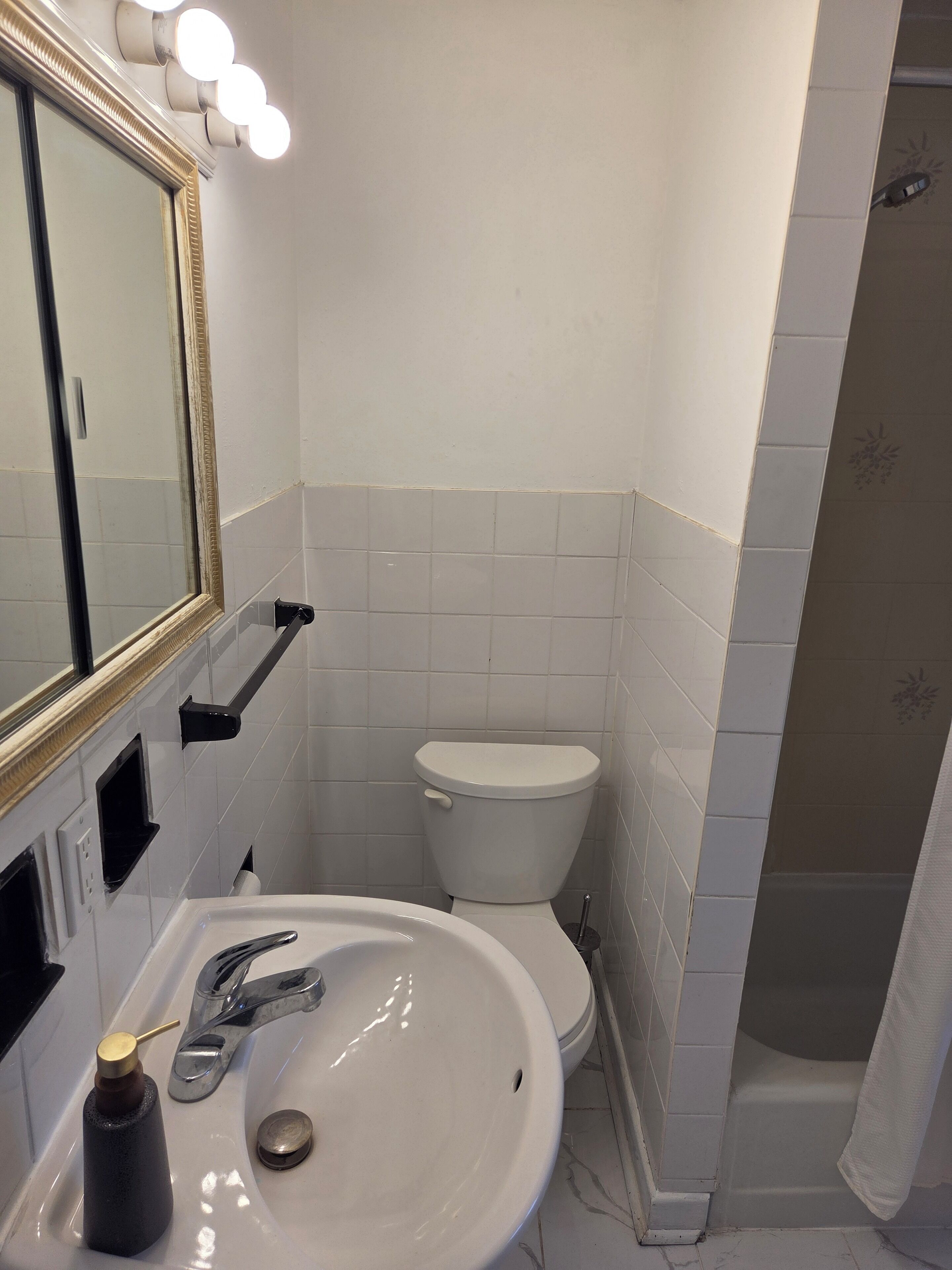 Un baño con lavamanos blanco, un espejo con iluminación, un inodoro y una zona de ducha.