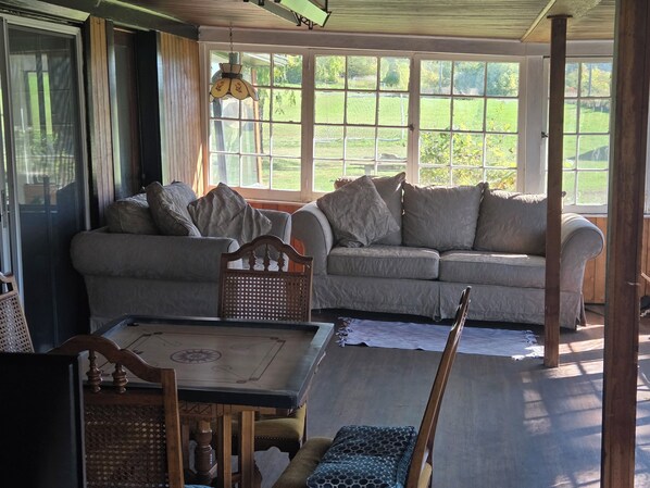 Un salon chaleureux avec deux canapés, une table en bois et une vue sur un paysage verdoyant grâce à de grandes fenêtres.