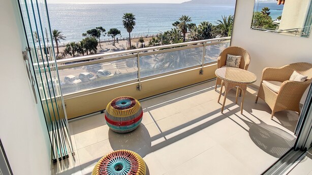 A balcony with a view of the sea, a wicker table and chairs, and two colorful stools. - Appartement Front de mer (Cannes)