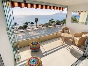 A balcony with a view of the sea, a wicker table and chairs, and two colorful stools. - Appartement Front de mer (Cannes)