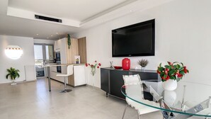 A modern kitchen with a dining area, a flat-screen TV mounted on the wall, and a glass table with chairs. - Appartement Front de mer (Cannes)