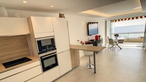 A modern kitchen with built-in appliances, a dining area with a view of the sea, and a balcony with outdoor seating. - Appartement Front de mer (Cannes)