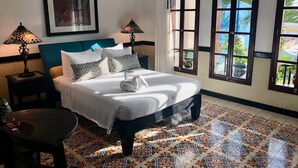 A neatly made bed with a white comforter and two pillows, a bedside table with a lamp, and a view of the outdoors through large windows. - Casa Sirena 8 Bedroom in Centro Villa with Pool, Walk Everywhere, Group Ready (Isla Mujeres)