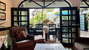 A cozy room with wicker furniture, a table, and a view of a lush garden through open doors. - Casa Sirena 8 Bedroom in Centro Villa with Pool, Walk Everywhere, Group Ready (Isla Mujeres)