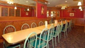 A restaurant with a long wooden table and green chairs, red walls, and ceiling fans.