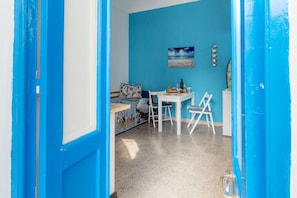 Une pièce avec un mur bleu, un lit avec un oreiller à rayures bleues et blanches, une petite table sur laquelle se trouvent un bol de fruits et une bouteille, et une chaise blanche.