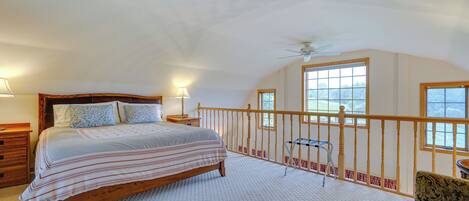Une chambre dotée d’un grand lit, d’une tête de lit en bois, d’un balcon avec une balustrade et offrant une vue sur l’extérieur.