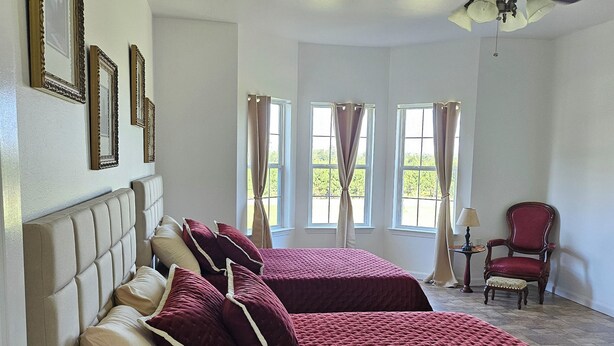 Ein Schlafzimmer mit zwei Betten, einem Deckenventilator und großen Fenstern mit Vorhängen.