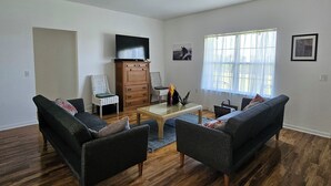 Ein Wohnzimmer mit zwei Sofas, einem Couchtisch, einem Fernseher auf einem Schrank und einem Deckenventilator.