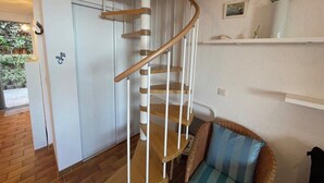 A spiral staircase in a room with a wicker chair and a white door. - Duplex in Pramousquier - sea view (Le Lavandou)