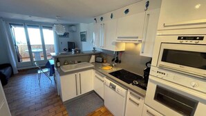 A compact kitchen with white cabinets, a dishwasher, a stove, and a microwave. - Duplex in Pramousquier - sea view (Le Lavandou)