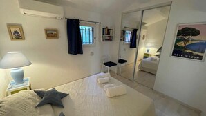 A hotel room with a bed, a nightstand with a lamp, a mirror, and a poster on the wall. - Duplex in Pramousquier - sea view (Le Lavandou)