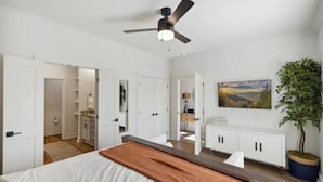 Un dormitorio con cama, ventilador de techo, un cuadro y planta en maceta.