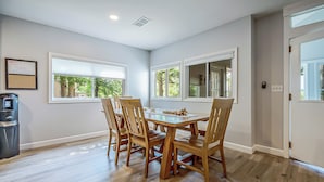 A dining room with a wooden table and chairs, large windows, and a water dispenser.