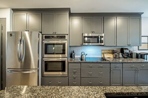 A modern kitchen with stainless steel appliances, granite countertops, and grey cabinetry.