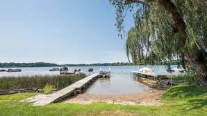 A lakeside dock with boats, a grassy area, and a tree.
