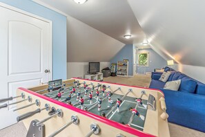 A room with a foosball table, a blue couch, and a television.