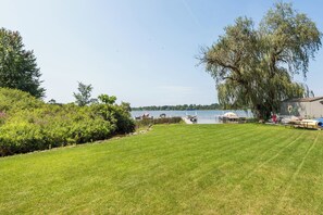 A grassy area with a lake, boats, and a large tree. - Cozy, quiet cottage on beautiful lake 30 minutes from Ann Arbor (Gregory)