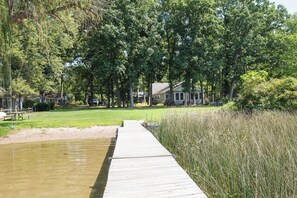 A wooden dock leading to a grassy area with a house in the background. - Cozy, quiet cottage on beautiful lake 30 minutes from Ann Arbor (Gregory)