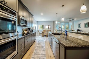 A modern kitchen with stainless steel appliances, a large island, and a dining area with wooden chairs.