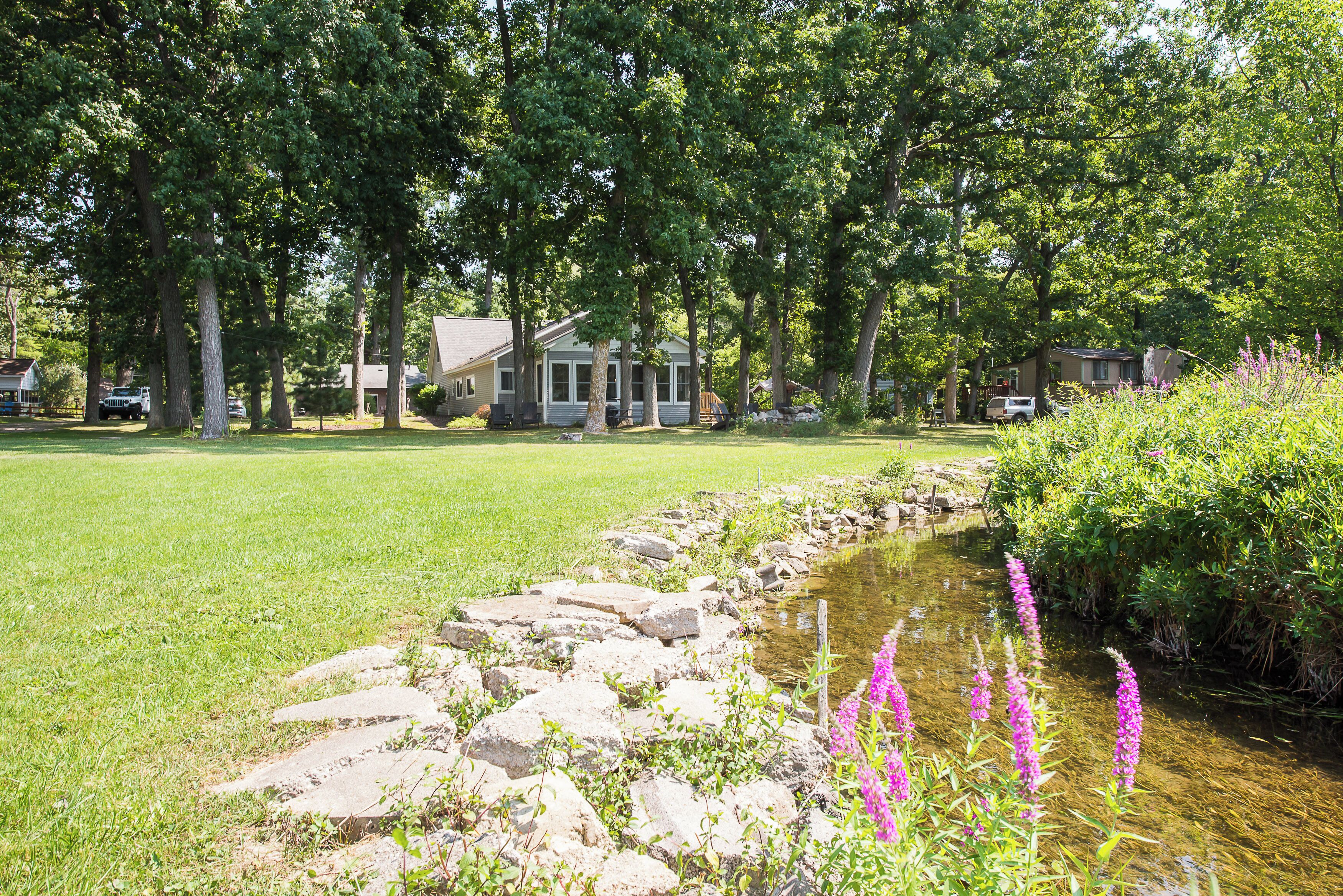 Un quartier résidentiel avec une pelouse verdoyante, un petit ruisseau et une rangée d’arbres.