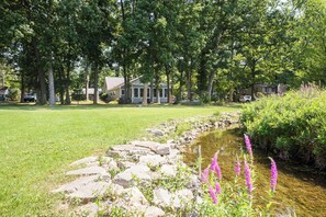 A residential area with a grassy lawn, a small stream, and a row of trees.