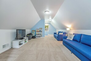 A spacious attic room with a television, bookshelf, and blue sofa.