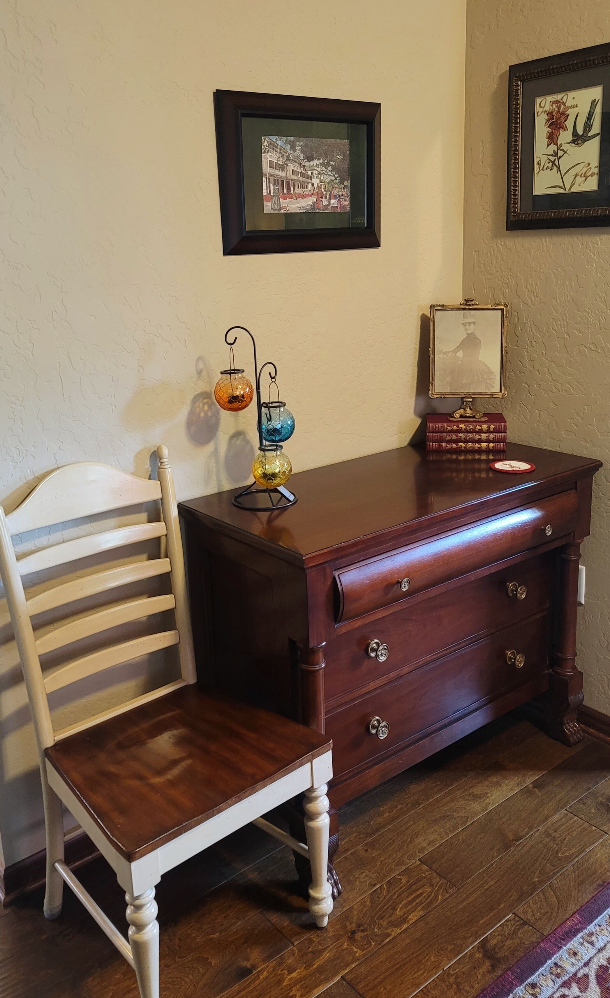 Une commode en bois avec des tiroirs, un tableau encadré accroché au mur et une chaise.
