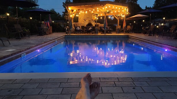 A swimming pool with a stone structure and string lights in the background. - Idyllic Cottage Memory Making with Pool & Outdoor Fireplace under the Gazebo, (Spokane Valley)