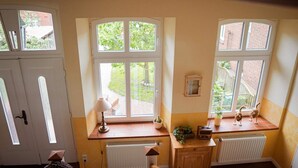 Ein Zimmer mit einer Holztreppe, einem Heizkörper, einer kleinen Kommode und einem Fenster mit Gartenblick.
