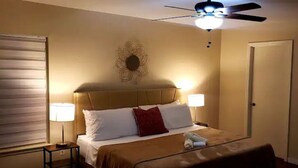 A hotel room with a bed, two bedside lamps, a ceiling fan, and a decorative wall piece.
