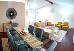 A modern living room with a glass dining table, blue chairs, a beige sofa with orange cushions, and yellow armchairs. - Eclectic Ranch Style Home - Sleeps 12 (Ocala)