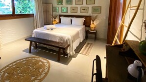 Un dormitorio con cama, mesitas de noche, un escritorio y una silla. Hay cuadros en la pared y una ventana con cortinas.