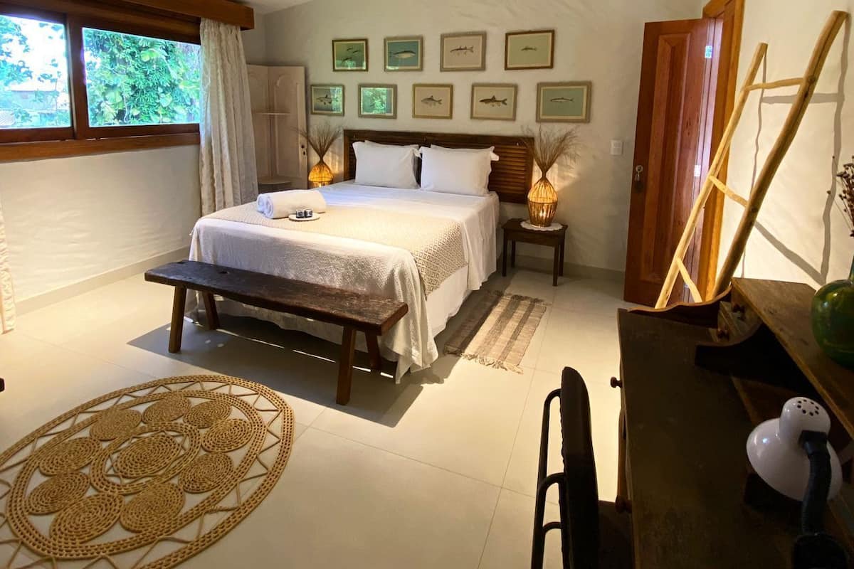 Une chambre à coucher avec un lit, des tables de chevet, un bureau et une chaise. Les murs sont ornés de tableaux encadrés et il y a une fenêtre avec des rideaux.