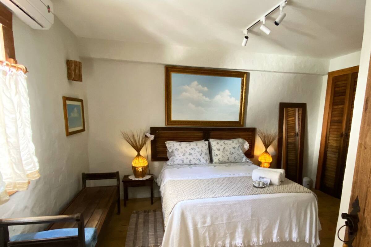 Une chambre à coucher avec un lit, des lampes de chevet, un banc en bois, un tapis et un ventilateur de plafond.