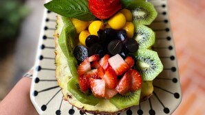 Una bandeja de frutas con fresas, kiwi, uvas y una piña sobre un plato decorativo.