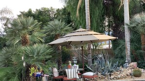 An outdoor patio with a table and chairs, surrounded by various plants and a pool. - NEW! Trendy hidden Gem / Private Room with Pool (Palm Desert)