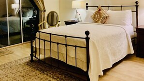 A bedroom with a bed, a ceiling fan, a window with blinds, a bedside table with a lamp, and a chair. - NEW! Trendy hidden Gem / Private Room with Pool (Palm Desert)