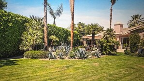 A well-maintained garden with palm trees, a patio, and a house with a tiled roof. - NEW! Trendy hidden Gem / Private Room with Pool (Palm Desert)