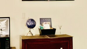 A room with a television mounted on the wall, a globe on a wooden cabinet, and a framed picture of a fern. - NEW! Trendy hidden Gem / Private Room with Pool (Palm Desert)