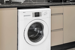 Un lave-linge BEKO à chargement frontal, de couleur blanche, se trouve dans une cuisine avec des armoires de couleur beige et un comptoir noir.