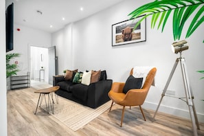 A modern living room with a black sofa, a wooden coffee table, a brown armchair, and a floor lamp. - Modern Apartment - On Street Parking - Rowley Regis (Halesowen)