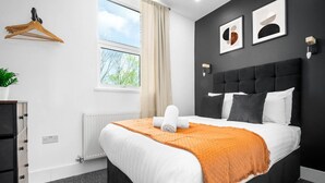 Ein modernes Hotelzimmer mit einem großen Bett, einem Heizkörper, einem Fenster mit Vorhängen, einer Pflanze und einer Wandleuchte.