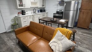 A compact kitchen with white cabinets, a stainless steel refrigerator, and a dining area with a wooden table and chairs. - Comfy, Clean & Pet Friendly (Gonzales)